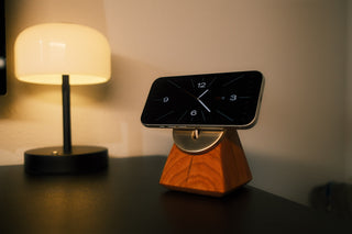 Smartphone on a stand with a digital clock display next to a lamp on a table.