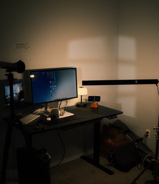 Dark room with a computer setup on a desk, including a monitor, keyboard, and mouse.