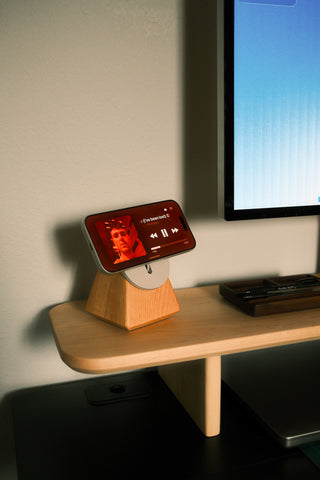 Phone on a wooden stand with a screen displaying a person, placed on a desk next to a computer monitor.