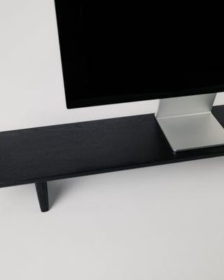 Close-up of Monolith Desk Shelf leg detail in black oak — handcrafted angled support with visible wood grain texture