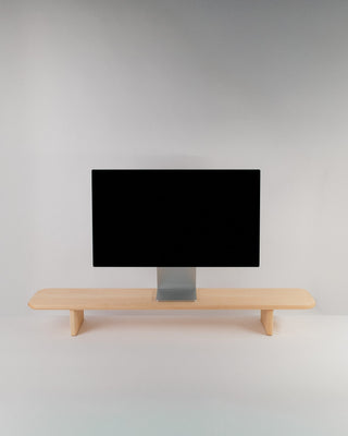 Monolith Desk Shelf in maple — solid hardwood monitor riser with rounded legs and softly curved edges, styled with an Apple Studio Display