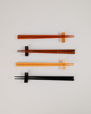 Four pairs of chopsticks resting on solid wood rests, side by side