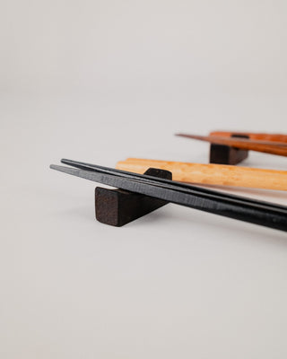 Two chopsticks resting on a single solid wood chopstick rest, angled view