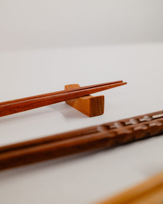 Close-up of patterned chopsticks resting on a solid cherry chopstick rest