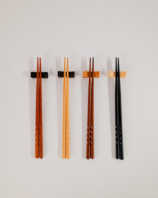 Four pairs of chopsticks resting on solid wood rests, full set view