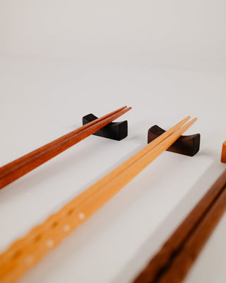 Close-up of two pairs of chopsticks resting on Indian laurel solid wood chopstick rests, styled on a light gray surface.