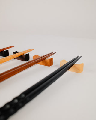 Two pairs of chopsticks resting on cherry wood rests, angled view